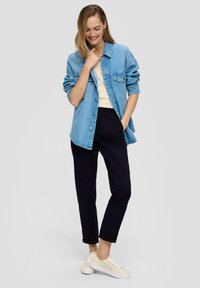 Chemise en denim bleu clair avec fermeture à boutons, haut crème, pantalon sombre et baskets beiges. Texture lisse, coupe décontractée, design casual.
