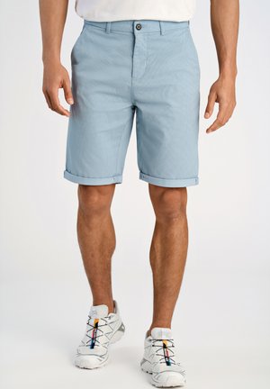 Lichtblauwe shorts met een gestructureerd patroon, voorzien van een knoopsluiting en omgerolde zoom. Gecombineerd met witte sportschoenen met meerkleurige veters.