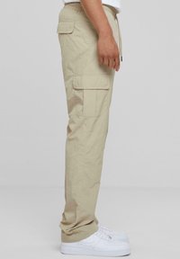 Beige cargobroek met een verstelbare tailleband, voorzien van zijzakken en een relaxte pasvorm. Gecombineerd met witte sneakers voor een casual uitstraling.