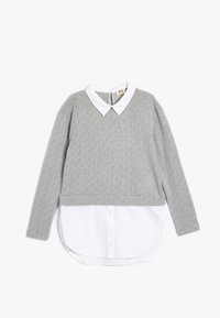 Suéter gris texturizado con una camisa blanca de cuello debajo. El suéter presenta un patrón de diamantes y un diseño cropped en la cintura.