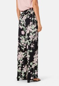 Pantalons fleuris noirs à coupe ample, avec des motifs de fleurs roses et vertes, une taille froncée et une texture fluide.