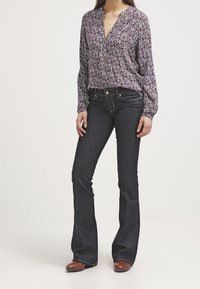 Blouse à manches longues florale dans des nuances de violet, associée à un jean bleu foncé évasé et des bottines brunes. Tissu lisse avec une coupe ample.