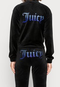 Black velour tracksuit featuring "Juicy" in rhinestones on the back of the jacket and rear of the pants. Slim-fit design with ribbed cuffs.