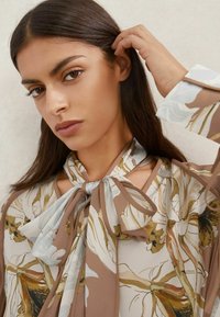 Lillemustriga pluus pehmest, voolavast kangast. Omaduseks lipsuga kaelus ja pikad varrukad kreemika ning maatoonides mustriga.