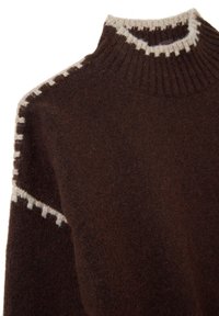 Pull en laine bouclée marron avec un col montant côtelé et des détails de couture crème sur le col et les bords des manches.