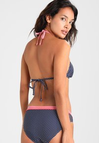 Laivastonsininen pilkullinen bikini punavalkoisilla raidoilla, jossa on solmittava kauluspanta ja keskitason alaosa, joka esittelee sileän kangasrakenteen.
