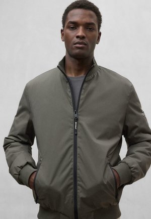Chaqueta bomber verde oliva con cremallera negra, puños acanalados y bolsillos laterales. Material suave con un cuello estructurado y acentos mínimos.