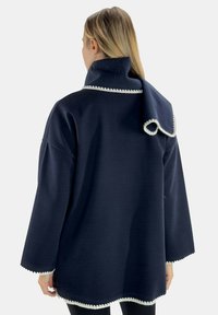Suéter de gran tamaño azul marino con un cuello alto, que presenta un borde blanco en forma de ondas a lo largo del escote y el dobladillo, hecho de un tejido texturizado.