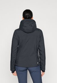 Giacca isolante nera con un ampio cappuccio, design aderente e polsini elasticizzati. Presenta un logo sull'orlo inferiore e una superficie esterna liscia.