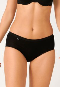 Boxer in cotone nero con una superficie liscia, caratterizzato da un bordo classico e da sottili bordi scallopati. L'etichetta con il logo è posizionata di lato.