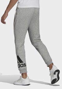 Szare dresowe spodnie z miękkiego materiału, o zwężanym kroju, z elastycznym pasem i dużym czarnym logo Adidas na lewej nodze.