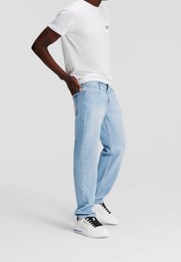 Vaqueros de denim de color azul claro con corte recto, combinados con una camiseta blanca lisa. Zapatillas blancas con acentos en negro completan el atuendo.