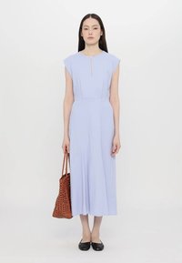 Rochie midi bleu deschis, cu mâneci scurte, decolteu în formă de cheie și material neted. Asortată cu o geantă maro din răchită și pantofi negri.