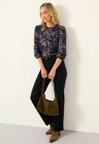 Marineblaues Oberteil mit floralem Muster und dreiviertel Puffärmeln, kombiniert mit dunklen Jeans und einer grünen Wildleder-Handtasche. Braune, mit Absatz versehene Stiefeletten.