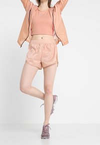 Kevyt, kiiltävä persikkavärinen takki vetoketjulla, siihen sopiva lyhyt toppi ja shortsit. Jalkineissa on violetteja yksityiskohtia ja läpinäkyvä pohja.