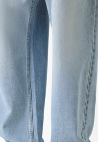 Svijetloplave traperice s vidljivim bočnim šavovima, ravnog kroja i blagim izbljeđenjem na bedrom, prikazane na neutralnoj pozadini.