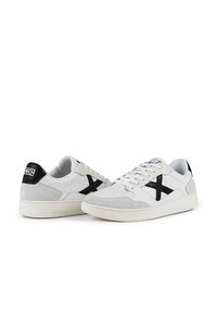 Sneaker in suede bianco con accenti neri, dotate di un logo nero a contrasto sul tallone, upper testurizzato e design con lacci.