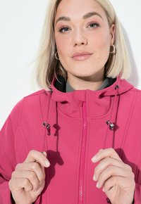 Fuchsiová zipová bunda s kapucí, stahovacími šňůrkami a hladkým povrchem. Obsahuje stříbrné kovové prvky a vysoký límec.