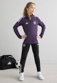 Purple zip-up sports top with white and black accents, paired with black pants featuring white stripes and logos. Soccer cleats and bag included.