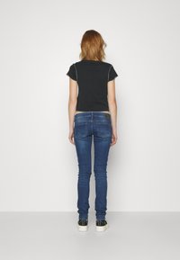 Camiseta negra corta con mangas cortas y costuras blancas, combinada con jeans ajustados azules y zapatillas negras con suelas blancas.