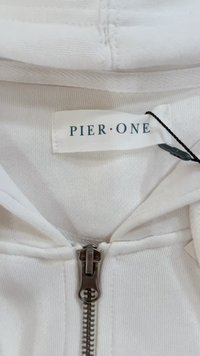 Le sweat à capuche zippé blanc présente une fermeture éclair argentée et une étiquette indiquant "PIER·ONE". Le tissu est doux et a une texture lisse.