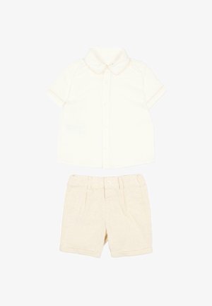 Maglietta per bambino a maniche corte color crema con bottoni frontali e pantaloncini beige coordinati con trama, bottoni e passanti per cintura.