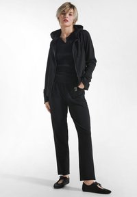 Costum sportiv negru format dintr-un hanorac cu fermoar, un top mulat și pantaloni lejeri. Material moale, cu detalii minime și textură subtilă.