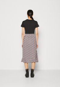 Haut noir à manches courtes associé à une jupe midi à motif floral dans des teintes de rose et de blanc, avec un ourlet évasé. Des bottes noires à semelles robustes complètent le look.