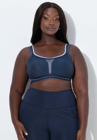 Marineblauwe sportbeha met een gaaspaneel, contrasterende stiksels en brede bandjes. Gecombineerd met marineblauwe, hoge taillelegging. Matte textuur.