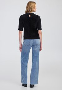 Czarny, puszysty sweter z krótkimi rękawami z dekoltem w kształcie łezki z tyłu, w połączeniu z jasnoniebieskimi dżinsami z wysokim stanem i czarnymi botkami na obcasie.