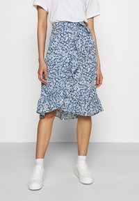 Blommig blå omslagskjol med volangkant, med små vita blommor och en figurnära midja. Kombinerad med vita sneakers.