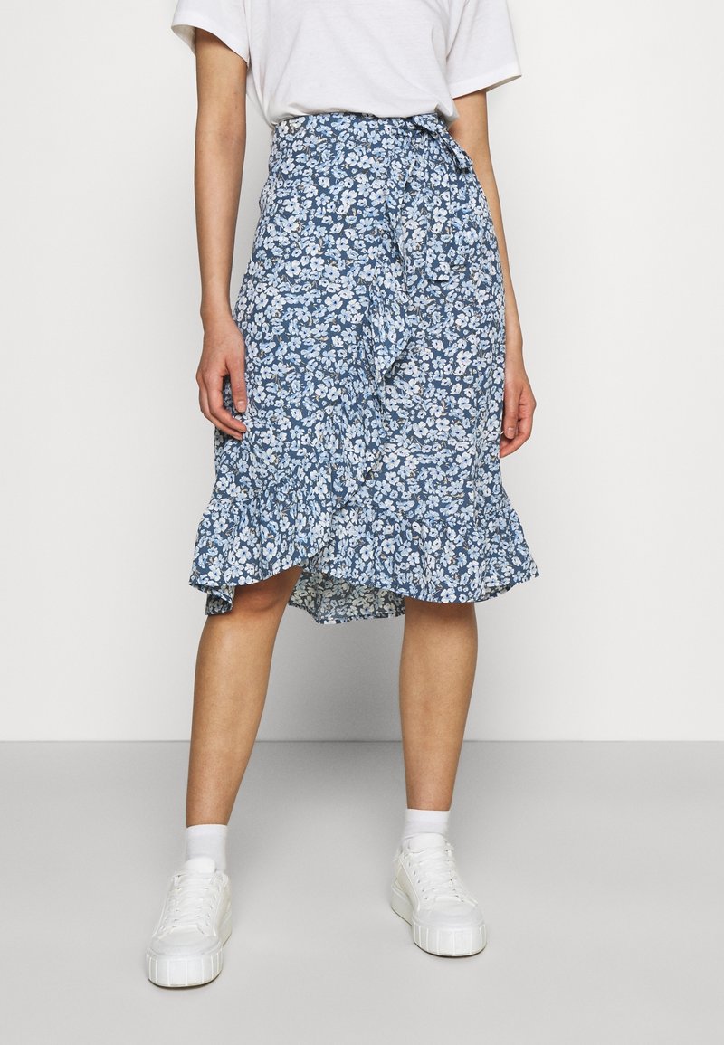 Blommig blå omslagskjol med volangkant, med små vita blommor och en figurnära midja. Kombinerad med vita sneakers.