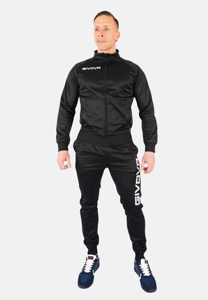 Black track suit made of shiny material, featuring a zip jacket with ribbed cuffs, and matching pants with a white logo on the side.