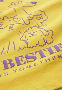 Kollane kangas, millel on lillad joonistused koertest ja lilledest koomikstil, kus on silmatorkavalt kirjas tekst "PARIMAD SÕBRAD ALATI KOOS".