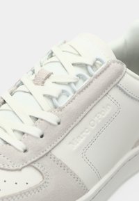 Witte sneaker met lichtgrijze suède accenten, ronde veters en gegraveerde merknaam. Soepele materialen, laag model, geperforeerde neus voor ventilatie.