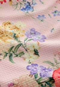 Blumenstoff mit pinkem Hintergrund und strukturierter Oberfläche; enthält gelbe, lila und weiße Blumen mit grünen Blättern.