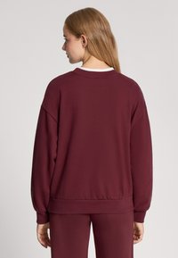 Bordowy sweter z okrągłym dekoltem, opuszczonymi ramionami i prążkowanymi mankietami. Miękka tekstura, luźny krój i subtelne detale szwów.