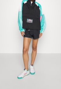 Černá a tyrkysová větrovka s polovičním zipem, velkou přední kapsou a elastickým lemem, doplněná černými šortkami a bílými teniskami s akcenty.