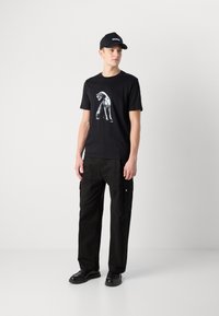 Black t-shirt with a graphic dog design, paired with black cargo pants. The outfit is complemented by a black cap featuring white text.