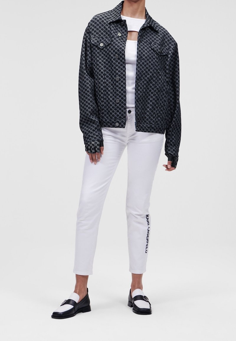 Black and white patterned denim jacket, white fitted top, white cuffed pants with logo, and black and white loafers. Textured fabric and casual fit.