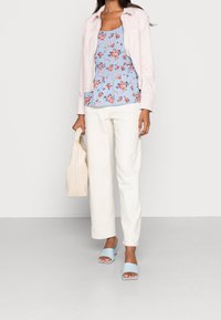Chemise boutonnée rose clair sur un top peplum à fleurs bleues, accompagnée d'un pantalon large blanc et de sandales à glissière bleu clair, tenant un sac crème.