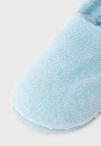 Gaiši zils vilnas čības ar mīkstu, teksturētu ārpusi un noapaļotu pirkstu dizainu. Zole ir plakana un gluda.