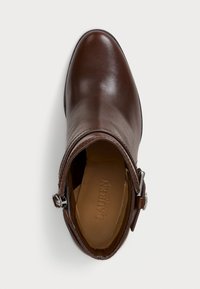 Bota de tornozelo em couro castanho com um acabamento liso, bico arredondado e um fecho de correr lateral. Apresenta uma faixa decorativa com ferragens metálicas.
