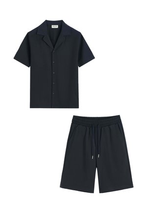 Chemise noire à manches courtes avec col et boutons, associée à un short noir à taille élastique avec cordon de serrage et poches latérales.