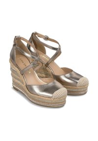 Scarpe a zeppa in oro metallico con tacco in juta intrecciata, punta rotonda e cinturini incrociati alla caviglia. La punta presenta un cappuccio testurizzato color crema.