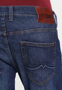 Jeans i denim med en mörkblå finish, med stickade detaljer, en lädermärkeslapp och en distinkt design på bakfickan.