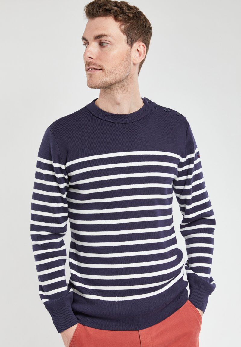 Pull navy à rayures avec des rayures horizontales blanches, col rond, détails de boutons à l'épaule, poignets et ourlet côtelés.