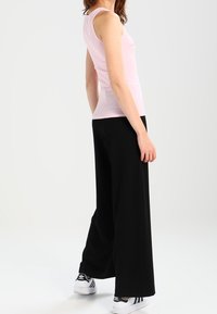 Haut rose sans manches associé à un pantalon noir ample avec une texture lisse. Des baskets blanches avec des accents noirs complètent la tenue.