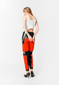 Top de tirantes blanco recortado combinado con pantalones bloqueados en naranja y negro que cuentan con paneles de cuero, textura elegante y cinturilla elástica.
