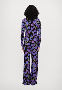 Kwiatowy kombinezon z długimi rękawami, z czarnym tłem i żywymi wzorami róż w odcieniach purpury i zieleni, szerokie nogawki oraz gładka faktura materiału.